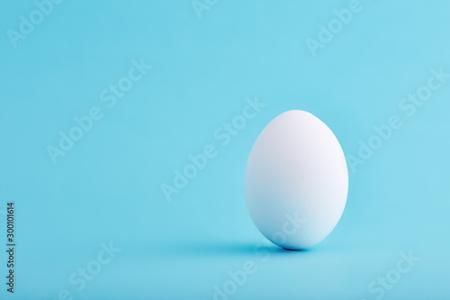 One white egg standing vertical on blue background