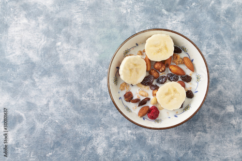 Bowl of granola with milk, nuts, raisins and banana. Concept for a tasty and healthy meal. Rustic wooden background. Top view. Copy space. 
