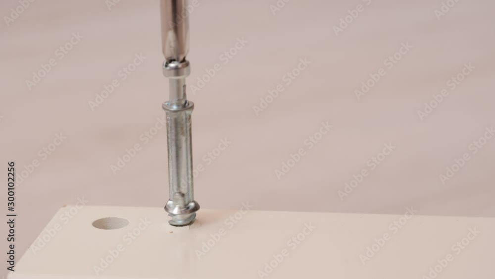 Assembling furniture at home. Mounting screw is screwed into hole board. Closeup of tool in hand. Do it yourself furniture assembly Assembling furniture at home. Mounting screw is screwed into hole board. Closeup of tool in hand. Do it yourself furniture assembly