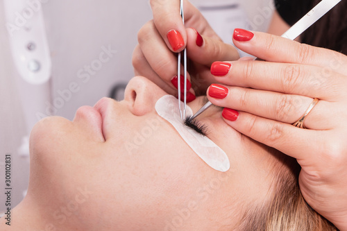 Eyelash Extension Procedure. Woman Eye with Long false Eyelashes. Closeup macro shot of fashion eyes in beauty salon. Hands beautician. 