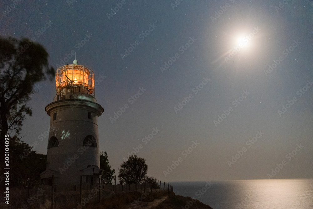 sea lighthouse on the shore at night with a bright moon in the night sky