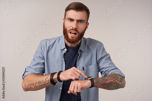 Canvas Print Grumpy blue-eyed brunette tattooed man with beard frowning his eyebrows while po