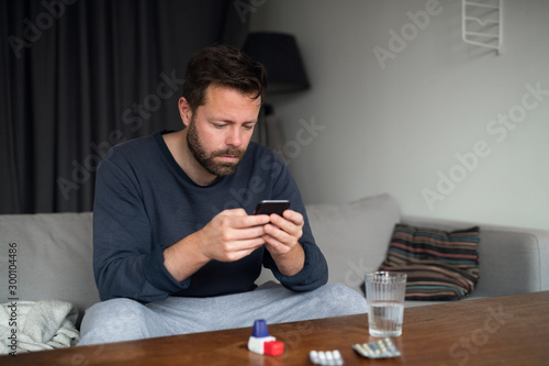 Man looking at phone after taking medicine while sick