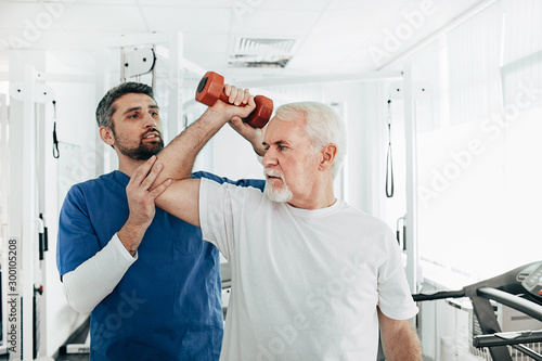 Valokuva senior man lift a dumbbell, he doing treatment exercise with his physiotherapist