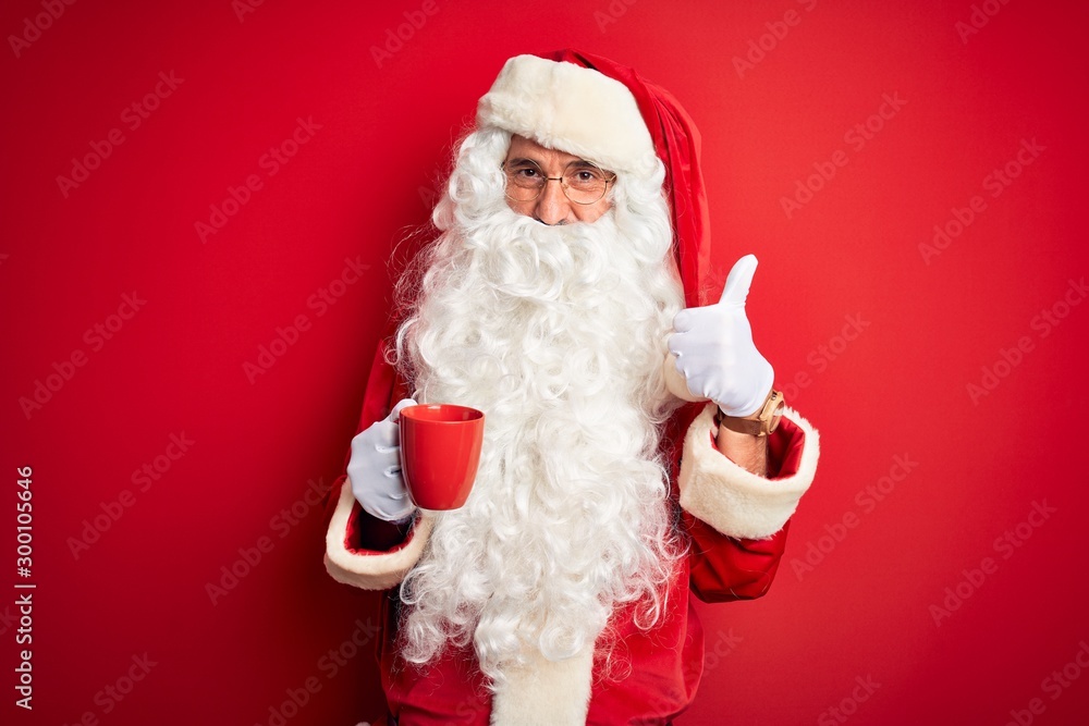 Senior man wearing Santa Claus costume holding cup of coffee over isolated red background happy with big smile doing ok sign, thumb up with fingers, excellent sign