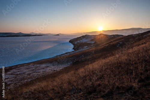 Sunset on Lake Baikal with ice in the winter. The sun sets over the mountains. The sky without clouds.