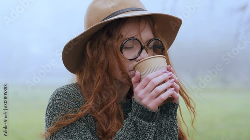 Portrait of young red hair woman drinkimg coffee in the park. Handheld shot. photo