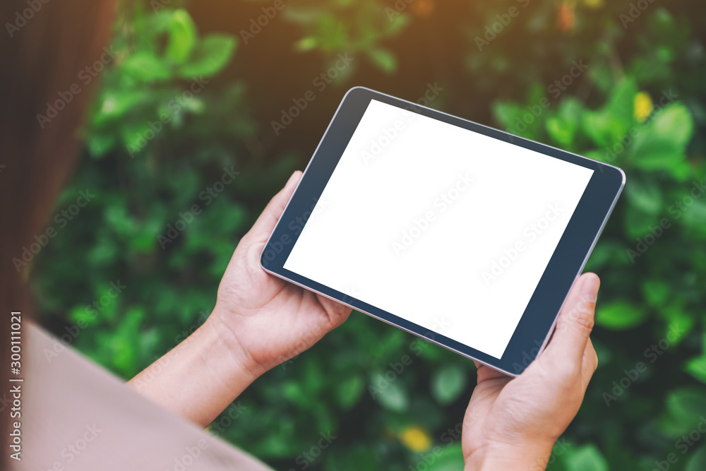 Mockup image of a woman holding black tablet pc with blank white desktop screen in the park