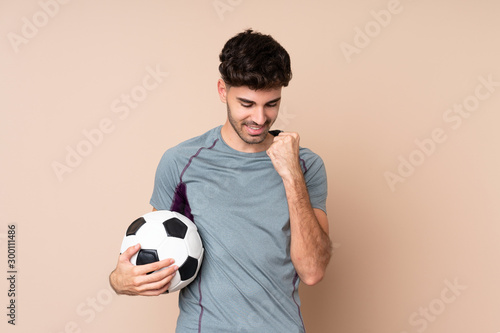 Young man over isolated background with soccer ball celebrating a victory