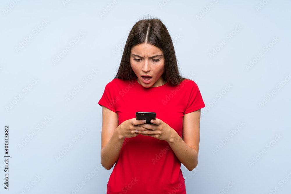 Naklejka premium Brunette young woman with a mobile phone over isolated blue wall