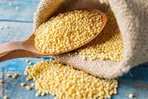 Raw yellow millet in a wooden spoon on burlap cloth on a background of blue rustic boards.
