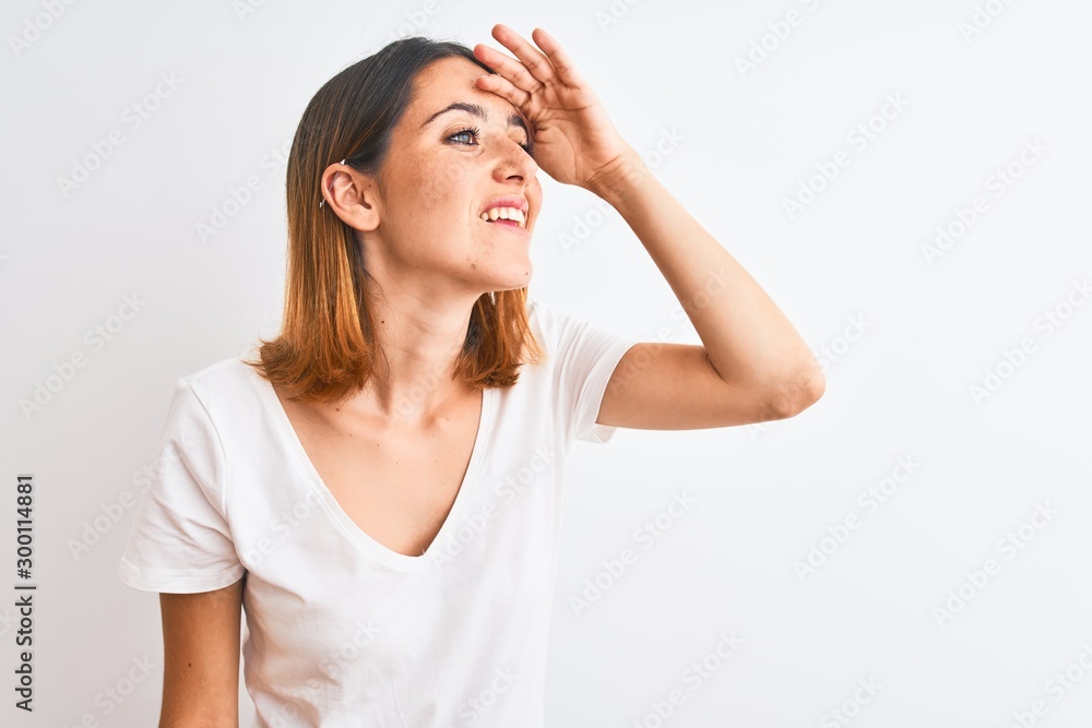 Beautiful redhead woman wearing casual white t-shirt over isolated background very happy and smiling looking far away with hand over head. Searching concept. Beautiful redhead woman wearing casual white t-shirt over isolated background very happy and smiling looking far away with hand over head. Searching concept.