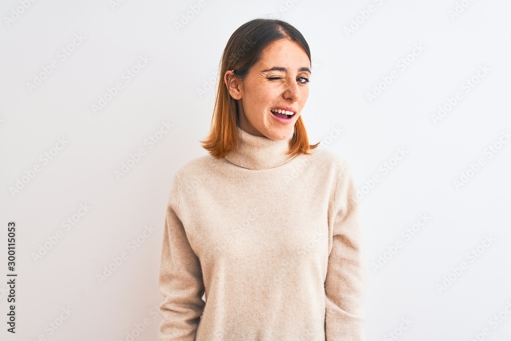 Beautiful redhead woman wearing winter turtleneck sweater over isolated background winking looking at the camera with sexy expression, cheerful and happy face. Beautiful redhead woman wearing winter turtleneck sweater over isolated background winking looking at the camera with sexy expression, cheerful and happy face.