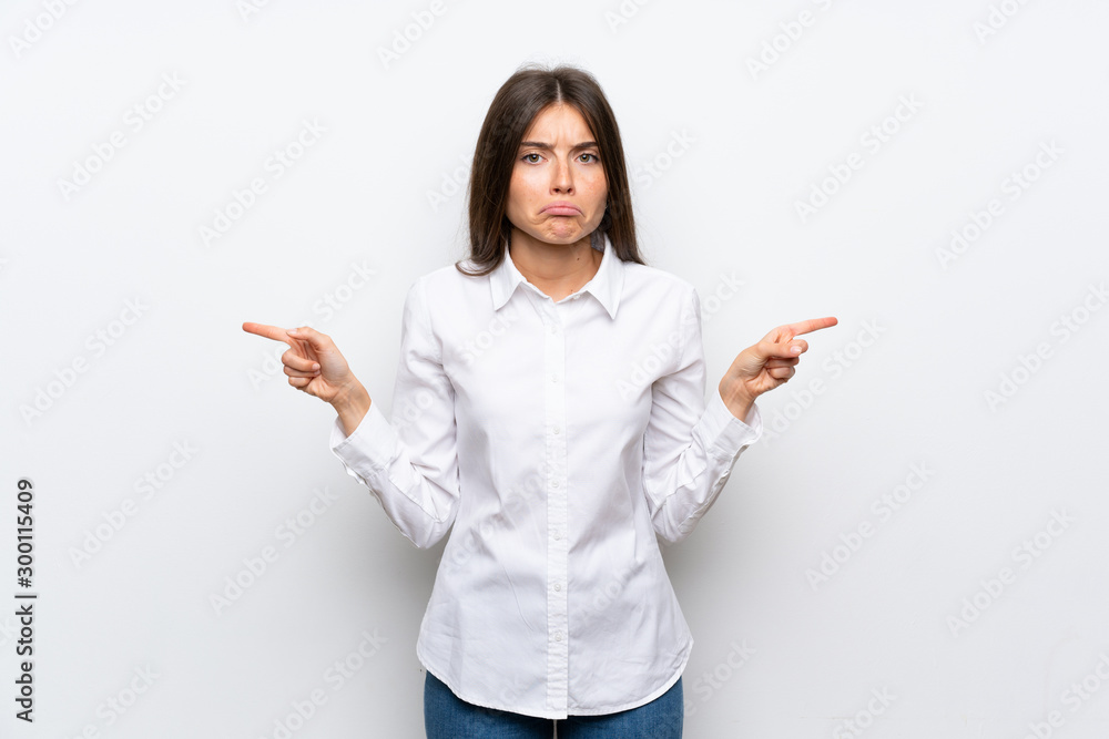 Young woman over isolated white background pointing to the laterals having doubts Young woman over isolated white background pointing to the laterals having doubts