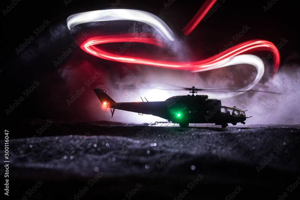 Silhouette of military helicopter ready to fly from conflict zone. Decorated night footage with helicopter starting in desert with foggy toned backlit. Selective focus. - obrazy, fototapety, plakaty 