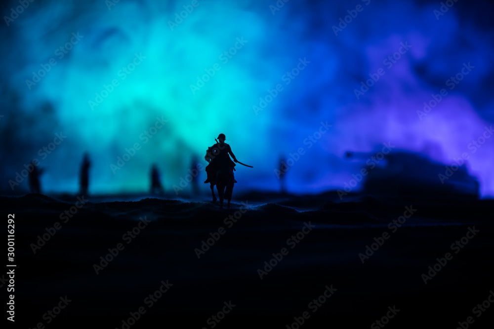 Fototapeta Oficer wojny światowej (lub wojownik) jeździec na koniu z mieczem gotowym do walki i żołnierzami na ciemnym, mglistym, stonowanym tle. Pole bitwy scena bitwy walczących żołnierzy.