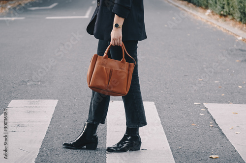 fashion blogger autumn 2019 outfit details. fashionable woman wearing black jeans, black ankle shoes a brown tan trendy leather handbag. crossing the street. detail of a perfect fall fashion outfit.  © mlasaimages