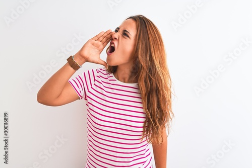 Young redhead woman wearing striped casual t-shirt stading over white isolated background shouting and screaming loud to side with hand on mouth. Communication concept.
