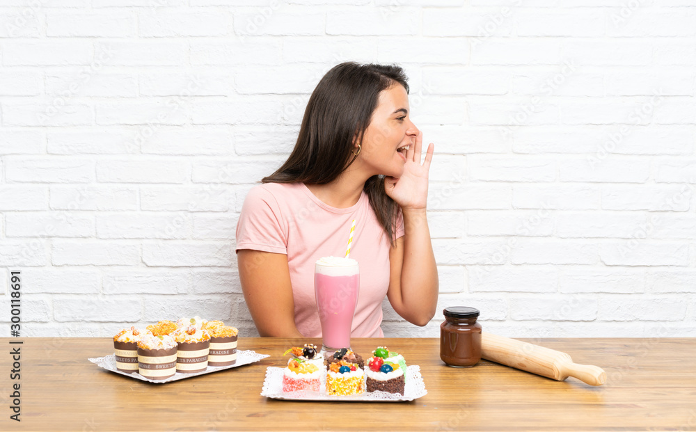 Young girl with lots of different mini cakes shouting with mouth wide open Young girl with lots of different mini cakes shouting with mouth wide open