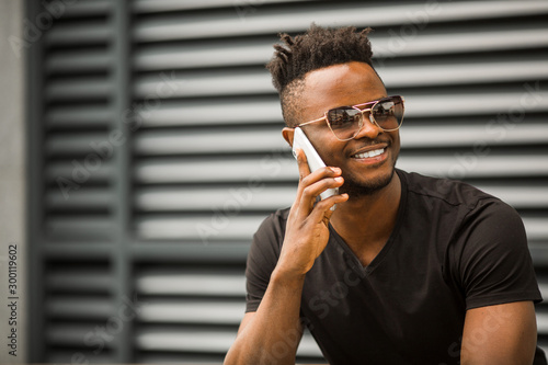 handsome young african man in a t-shirt and glasses phoning