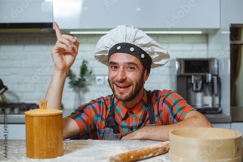 Happy man in the kitchen looks with his finger up at a table with flour.