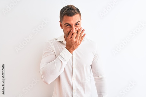 Young handsome business man wearing elegant shirt over isolated background smelling something stinky and disgusting, intolerable smell, holding breath with fingers on nose. Bad smells concept.