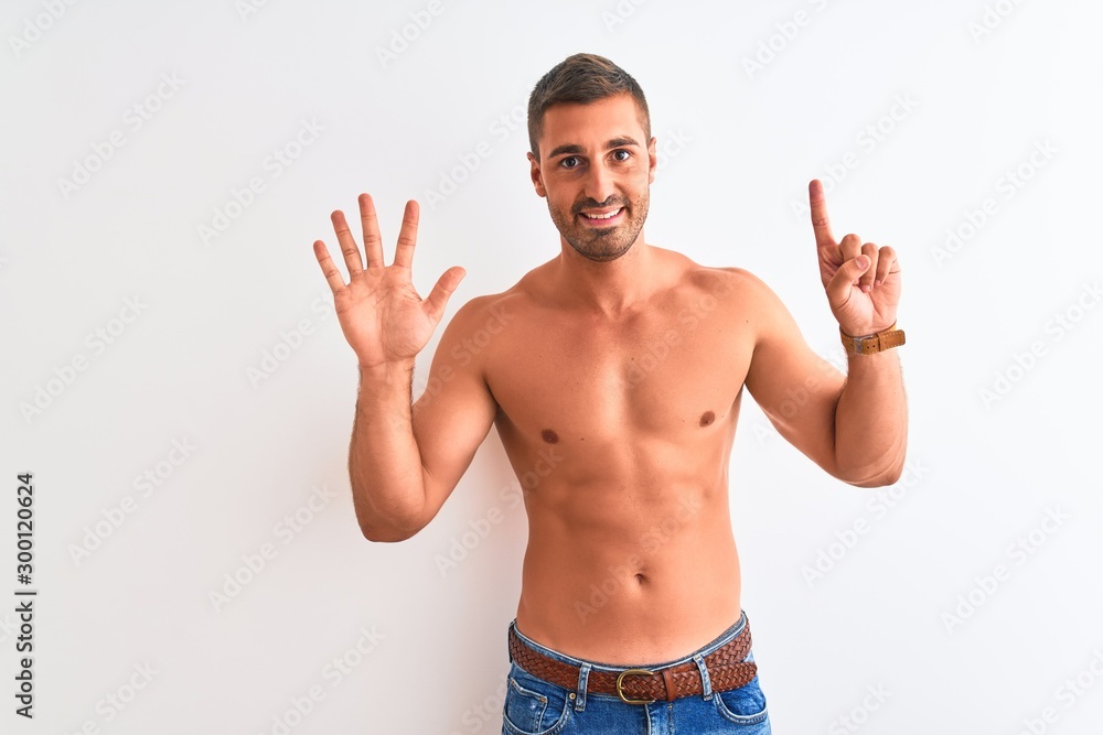 Young handsome shirtless man showing muscular body over isolated background showing and pointing up with fingers number six while smiling confident and happy.