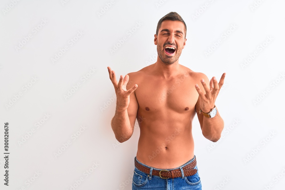 Young handsome shirtless man showing muscular body over isolated background crazy and mad shouting and yelling with aggressive expression and arms raised. Frustration concept.