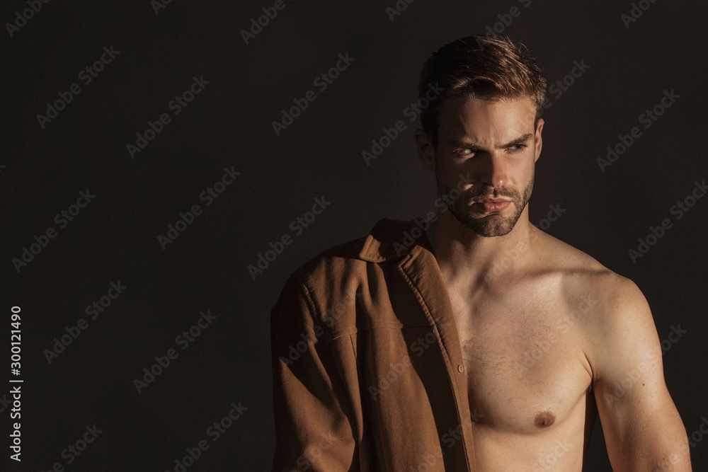 Naklejka premium Muscle strong beautiful stripped male model with brown coat in denim blue jeans in glasses eyewear on black isolated font background