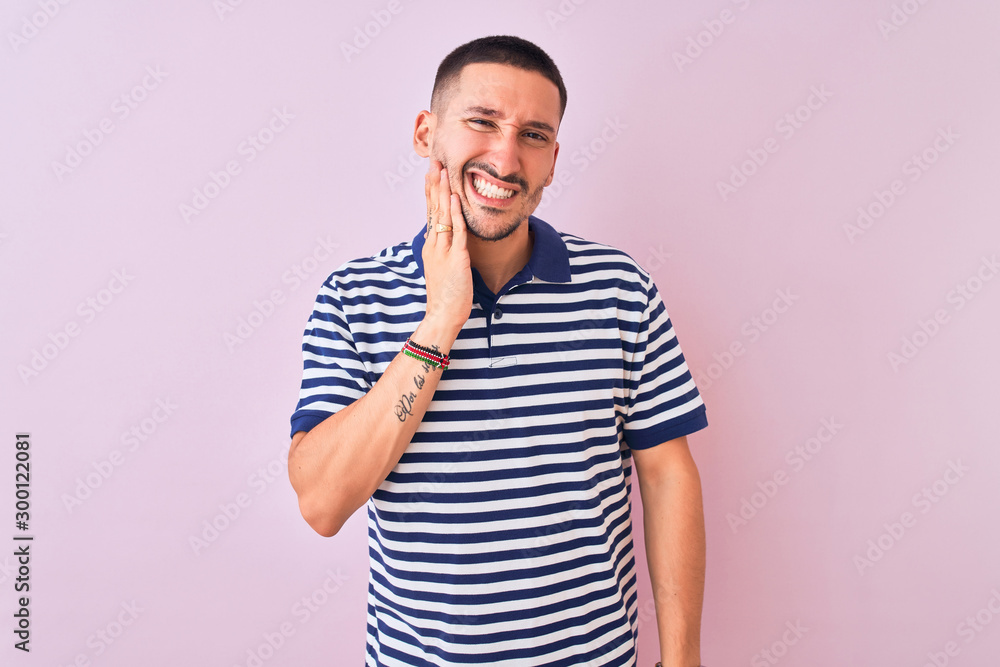 Young handsome man wearing nautical striped t-shirt over pink isolated background touching mouth with hand with painful expression because of toothache or dental illness on teeth. Dentist concept. Young handsome man wearing nautical striped t-shirt over pink isolated background touching mouth with hand with painful expression because of toothache or dental illness on teeth. Dentist concept.