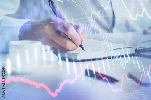 Double exposure of man's hands writing notes of stock market with forex chart.