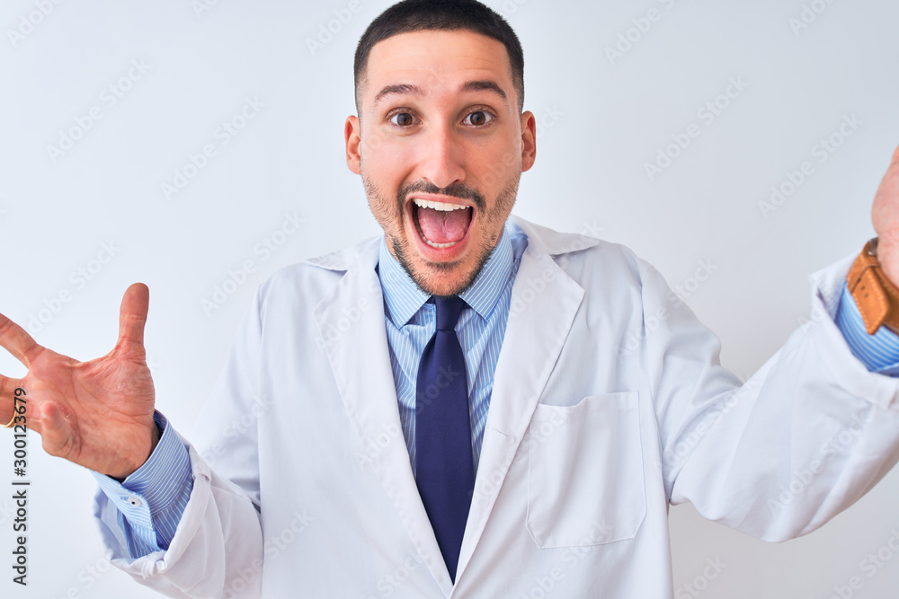 Young doctor man wearing white coat over isolated background celebrating crazy and amazed for success with arms raised and open eyes screaming excited. Winner concept Young doctor man wearing white coat over isolated background celebrating crazy and amazed for success with arms raised and open eyes screaming excited. Winner concept