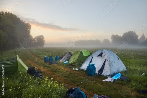 Tents on a field in early morning mist, dramatic sunrise glow on the horizon