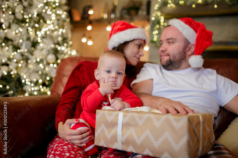 Image of young parents in Santa's caps with son sitting in chair in room . Image of young parents in Santa's caps with son sitting in chair in room .