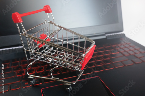 Shopping online concept - shopping cart on the black keyboard. Red mettal trolley on a laptop keyboard. Shopping service on the online web. Offers home delivery. Copyspace for text.
