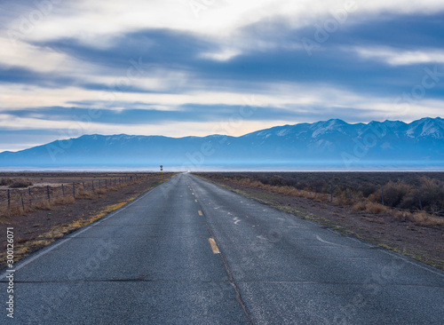 The road goes to the horizon against the background of the morning cloudy sky and mountains