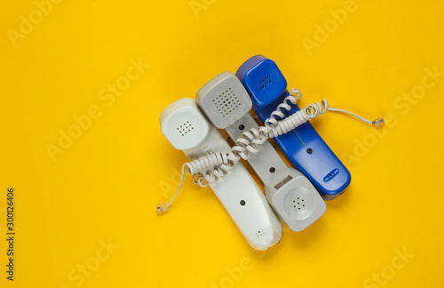 Three office phone tubes wrapped in cable on yellow studio background. Call center, hotline concept photo