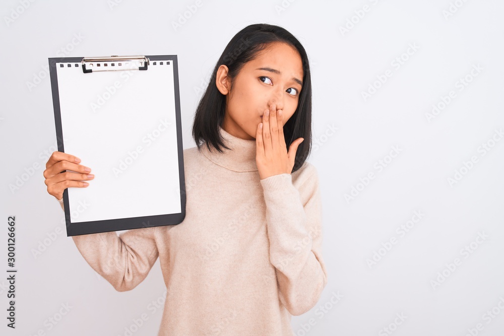 Young chinese inspector woman holding clipboard standing over isolated white background cover mouth with hand shocked with shame for mistake, expression of fear, scared in silence, secret concept