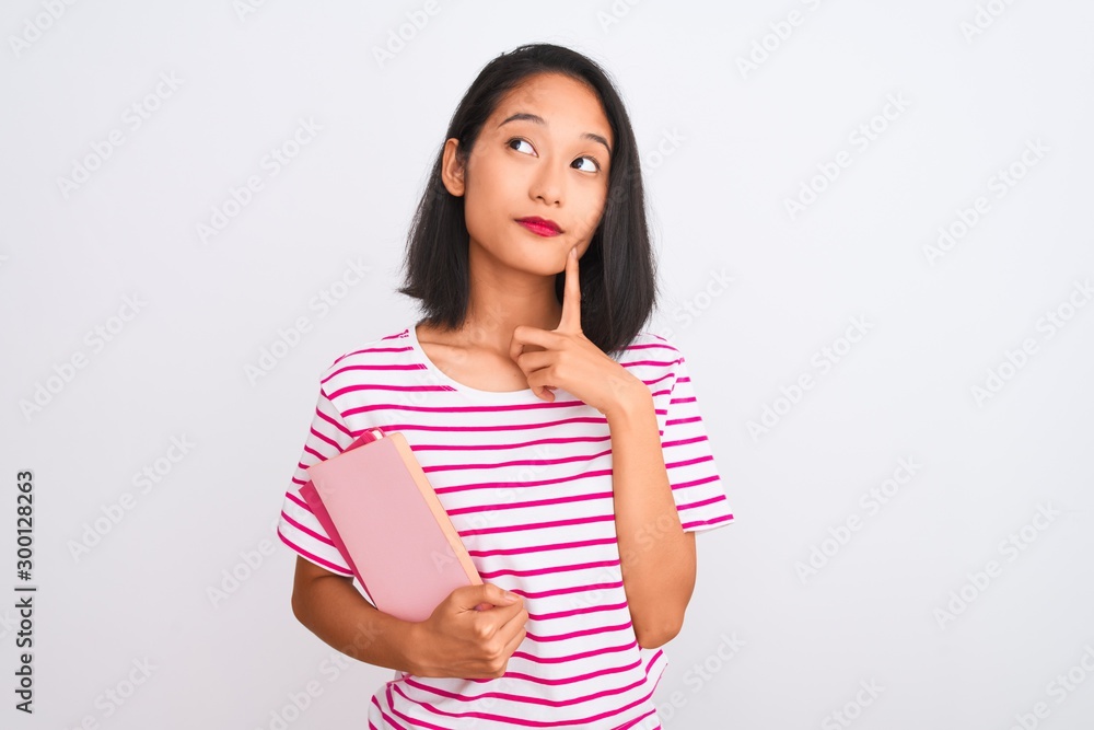 Young beautiful chinese woman holding books standing over isolated white background serious face thinking about question, very confused idea Young beautiful chinese woman holding books standing over isolated white background serious face thinking about question, very confused idea
