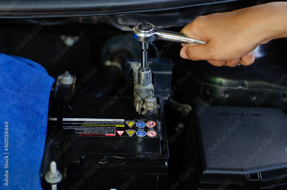 A woman using a wrench to change the car battery
