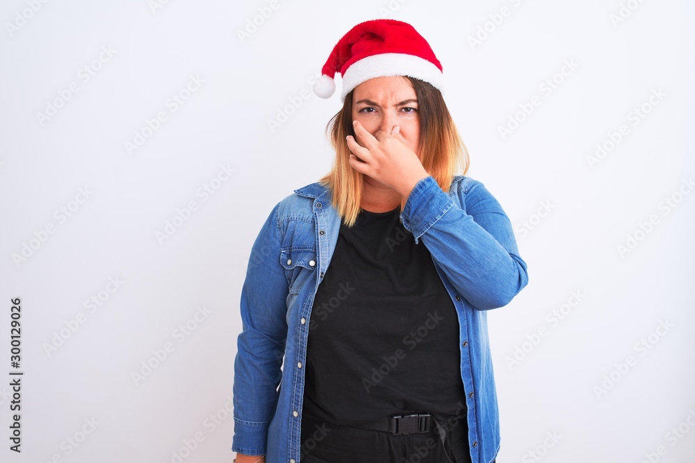 Young beautiful woman wearing Christmas Santa hat standing over isolated white background smelling something stinky and disgusting, intolerable smell, holding breath with fingers on nose. Bad smell Young beautiful woman wearing Christmas Santa hat standing over isolated white background smelling something stinky and disgusting, intolerable smell, holding breath with fingers on nose. Bad smell