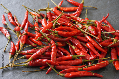 Close-up image of a pile of hot Thai bird chiles on a gray slate background
