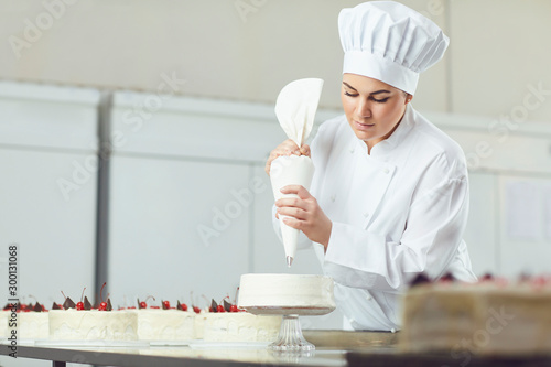 Schilderij op canvas Confectioner decorating cake in pastry shop.