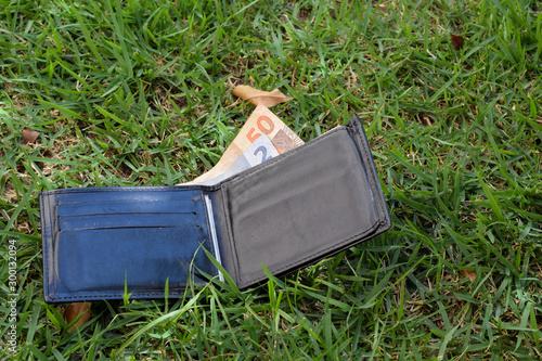 black wallet with brazilian money banknotes fallen on the grass