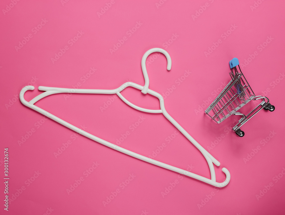 Plastic hanger and shopping trolley on pink paper background. Minimalistic fashion concept. Top view Plastic hanger and shopping trolley on pink paper background. Minimalistic fashion concept. Top view