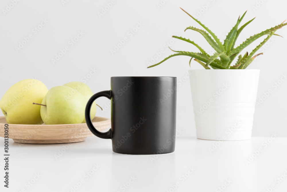 Black mug mockup with apples and a aloe vera plant on a white table. Black mug mockup with apples and a aloe vera plant on a white table.