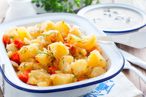 Baked sliced potatoes with carrots and onions in an enameled form, horizontal