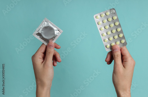 Принти на полотні Hand holds condoms in packaging, birth control pills on blue  background