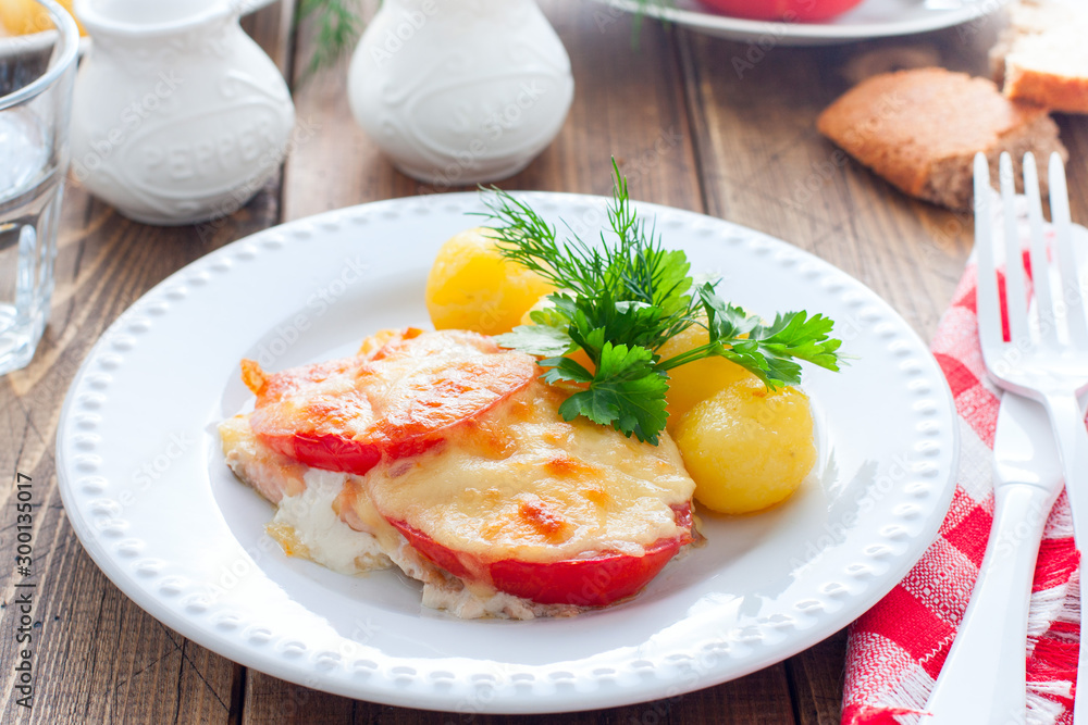 Baked pink salmon with tomato and cheese on a white plate with potatoes, horizontal Baked pink salmon with tomato and cheese on a white plate with potatoes, horizontal