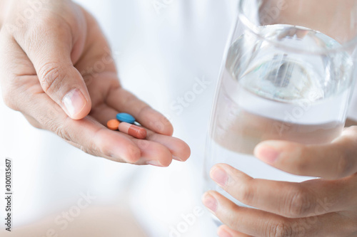 Closeup woman hand holding pills and glass of water, health care and medical concept, selective focus